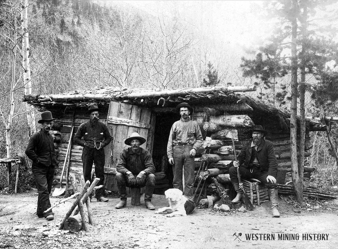 Miners pose with dog at their cabin somewhere in Colorado